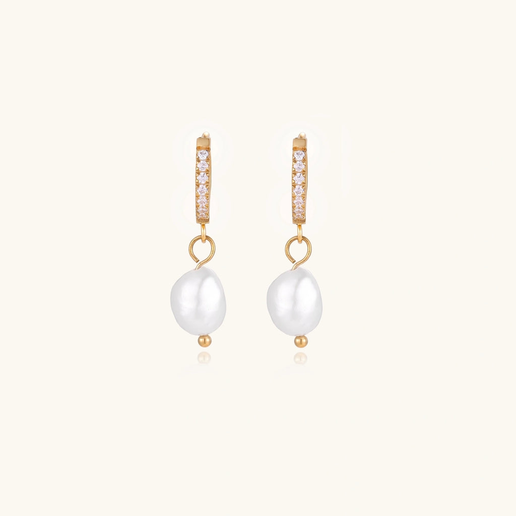 Gold huggie hoop earrings with pavé crystals and white freshwater pearl drops on cream background