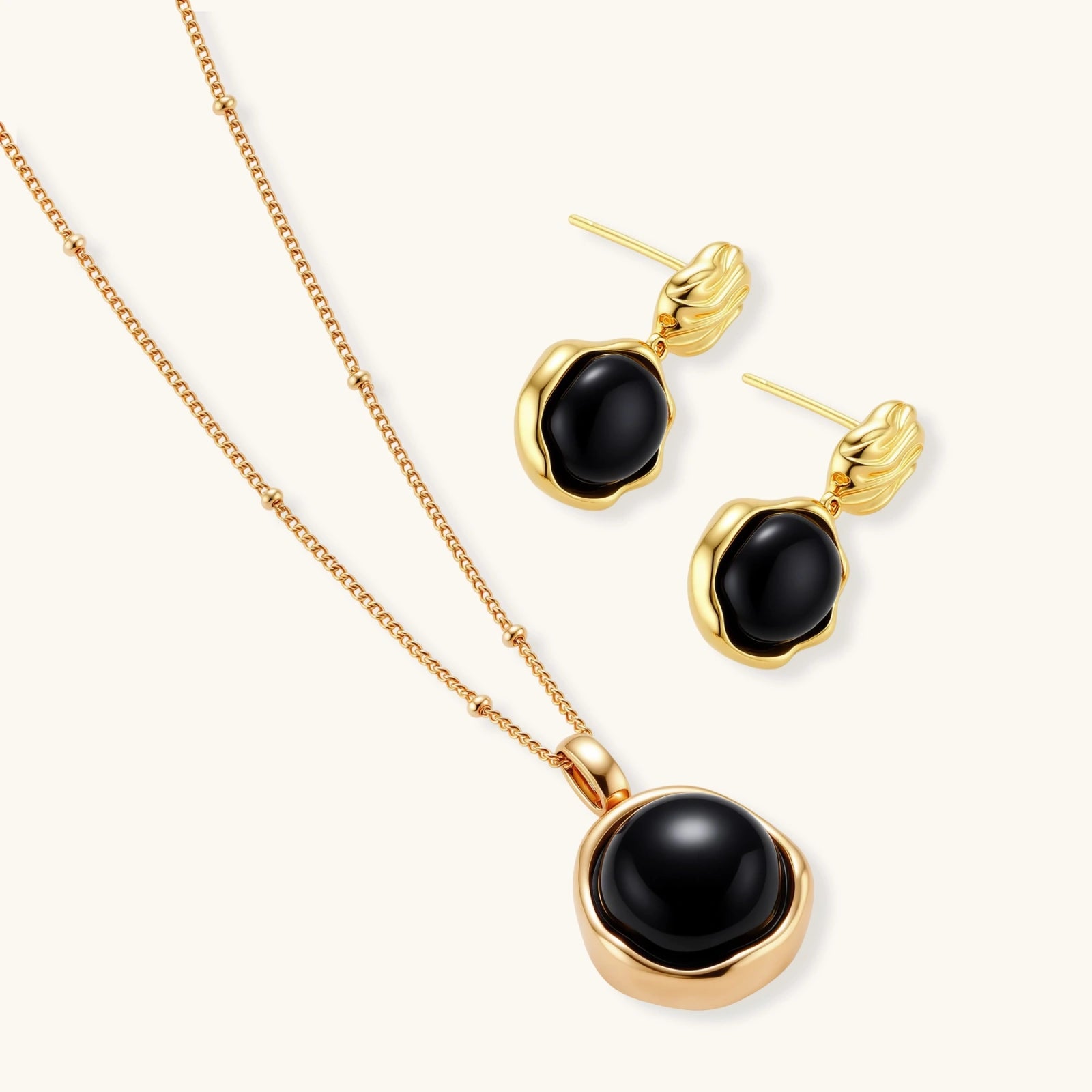 Circular black agate pendant on gold-plated sterling silver chain against cream background, showing modern minimalist design.