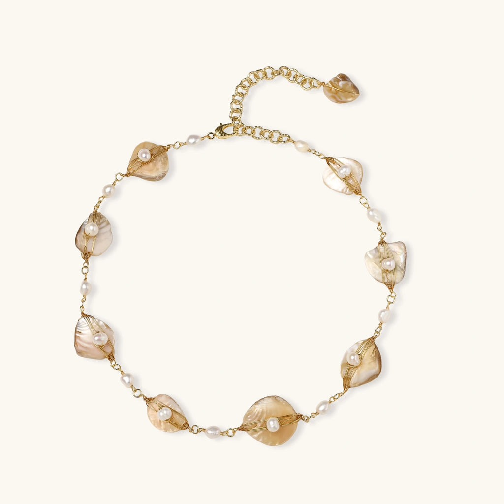 Gold-plated necklace with wire-wrapped shell pieces and freshwater pearls on neutral background, adjustable chain visible.
