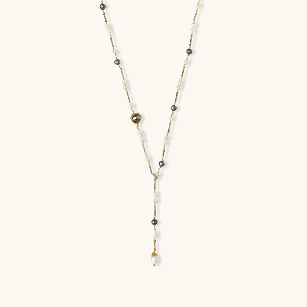 Y-shaped gold-plated necklace with white and gray freshwater pearls on cream background, showing adjustable drop design.