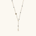 Y-shaped gold-plated necklace with white and gray freshwater pearls on cream background, showing adjustable drop design.