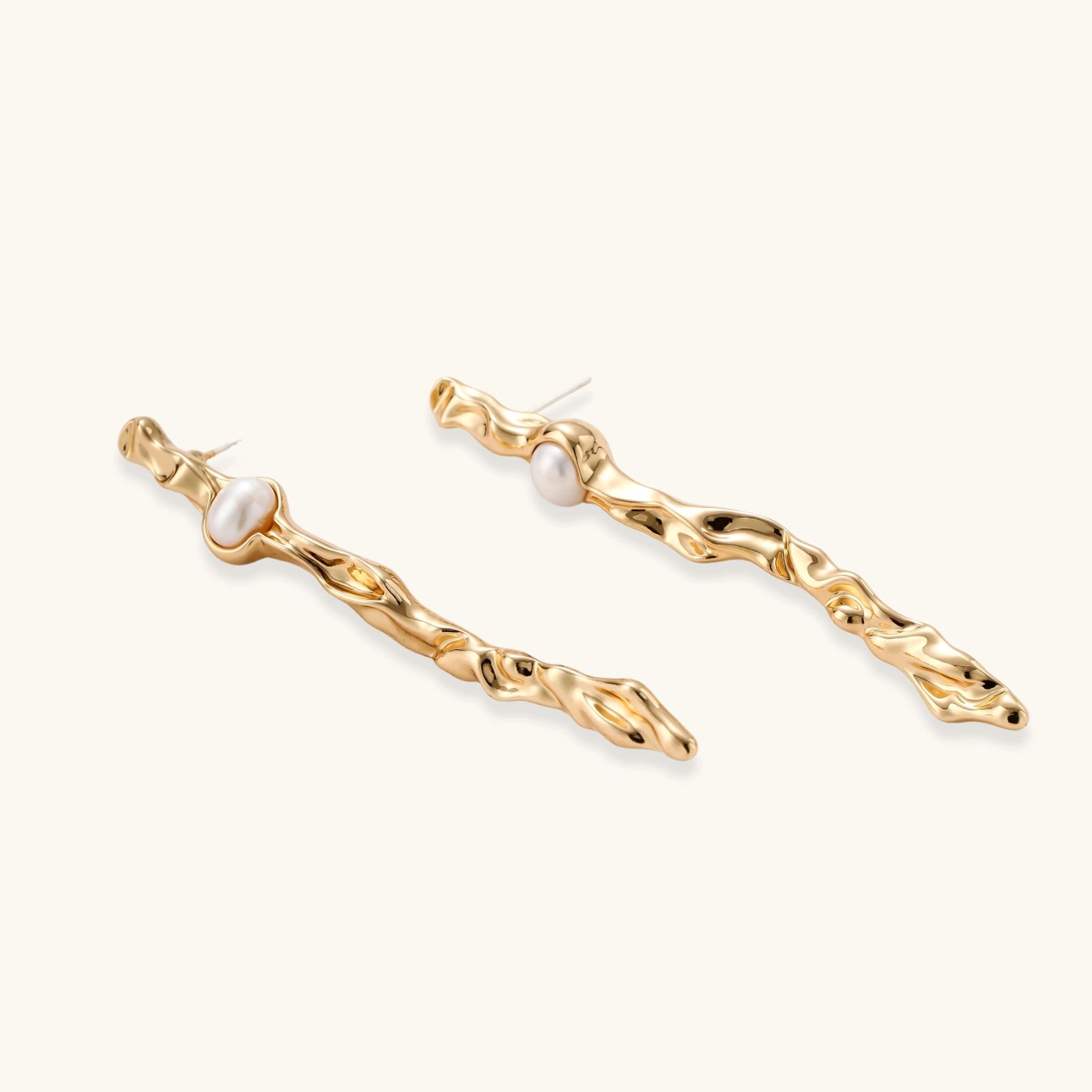 Organic twisted gold-toned drop earrings with white ABS pearls positioned near the top on cream background.