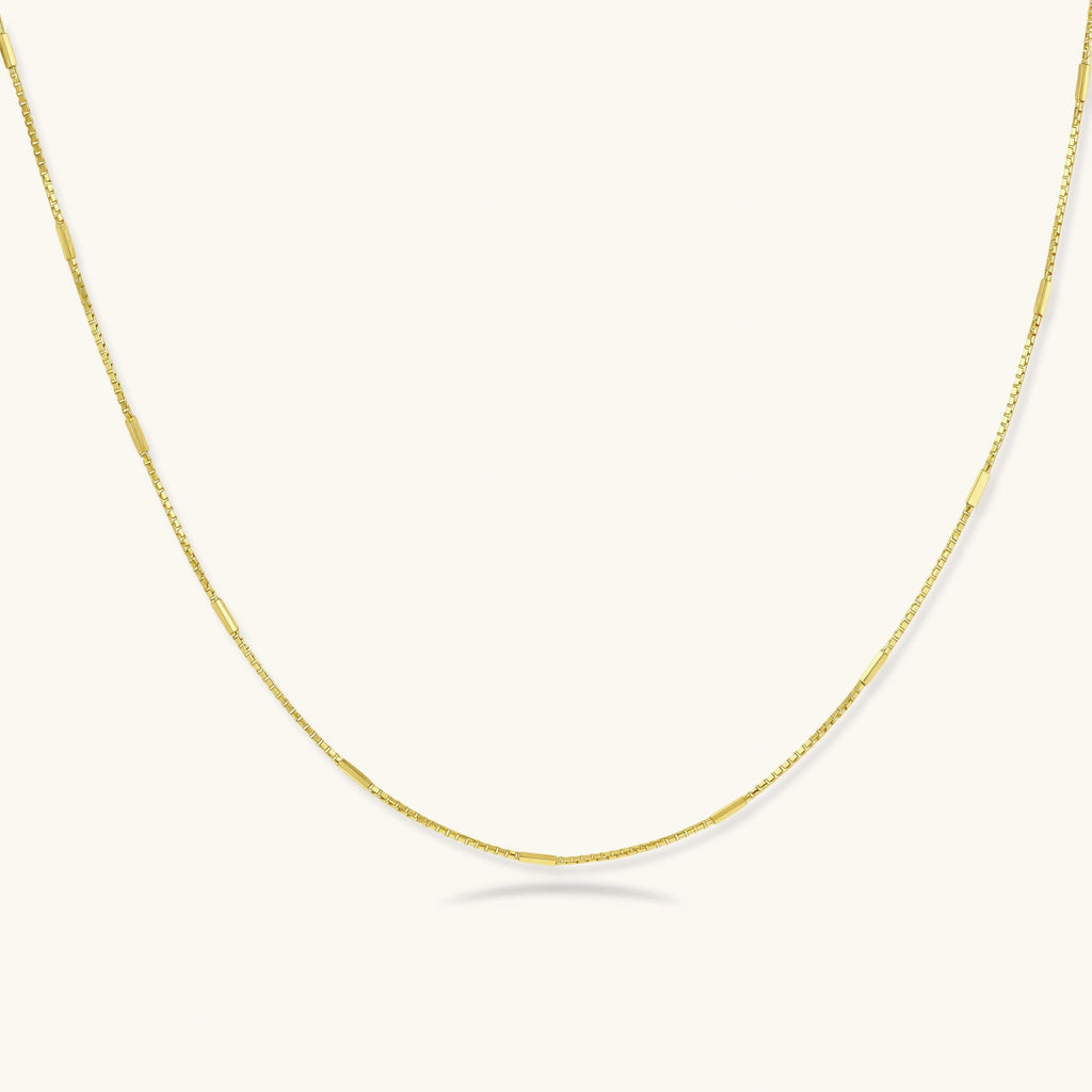 Delicate gold-plated sterling silver chain necklace with geometric segments displayed against cream background