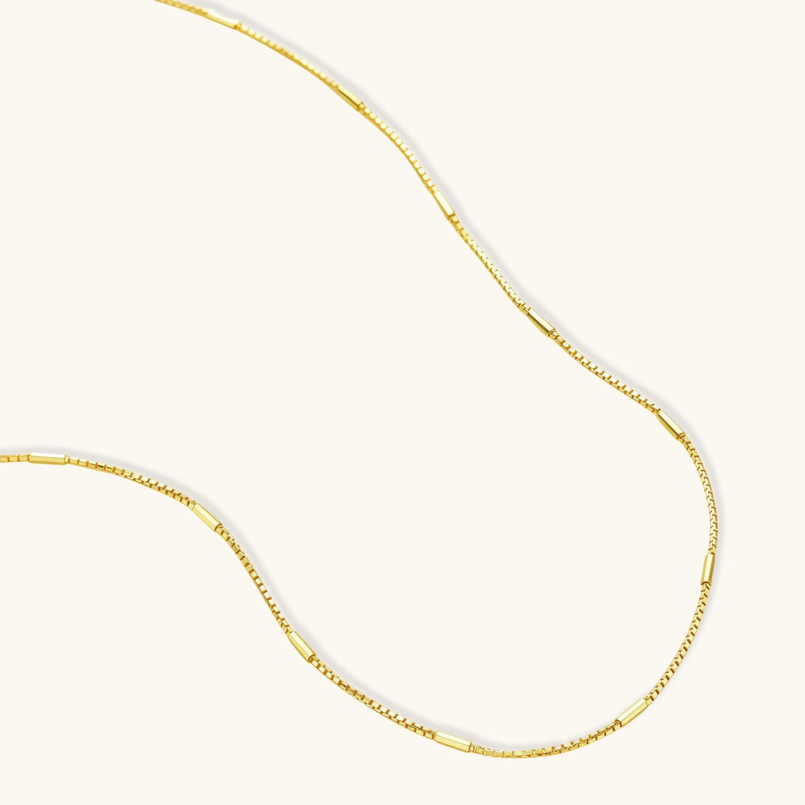 Delicate gold-plated sterling silver chain necklace with geometric segments displayed against cream background