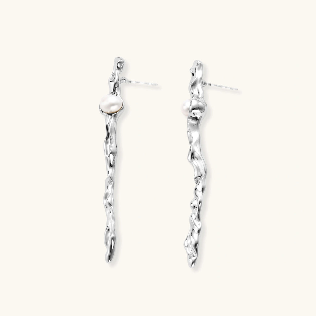 Sculptural silver drop earrings with flowing twisted design and white pearls on neutral background.