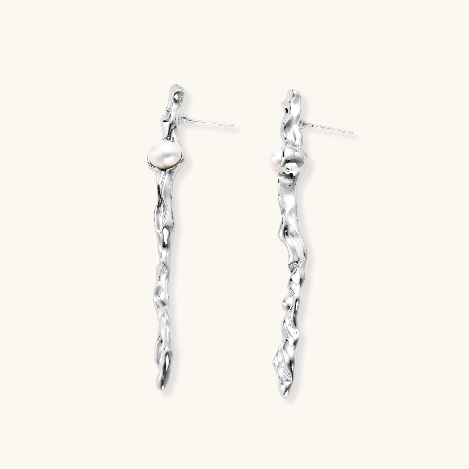 Sculptural silver drop earrings with flowing twisted design and white pearls on neutral background.