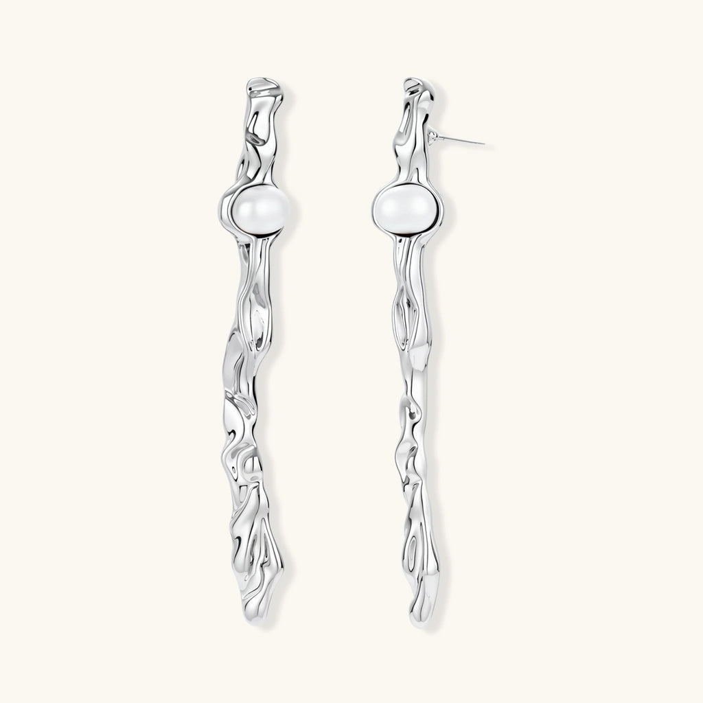 Sculptural silver drop earrings with flowing twisted design and white pearls on neutral background.