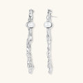 Sculptural silver drop earrings with flowing twisted design and white pearls on neutral background.