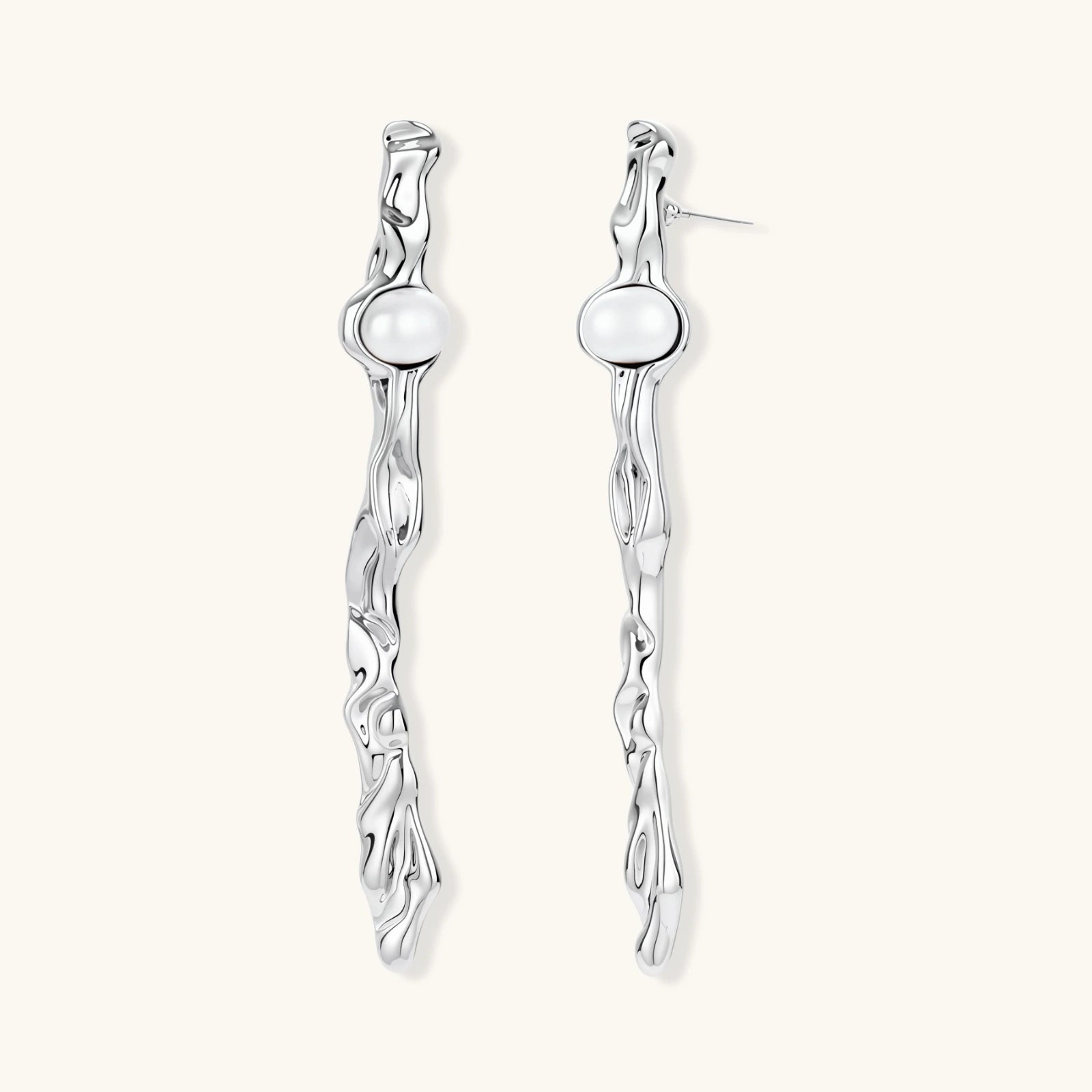 Sculptural silver drop earrings with flowing twisted design and white pearls on neutral background.