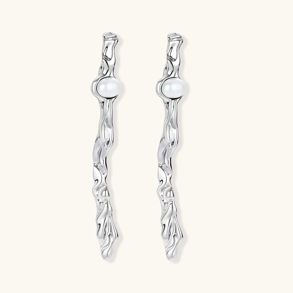 Sculptural silver drop earrings with flowing twisted design and white pearls on neutral background.