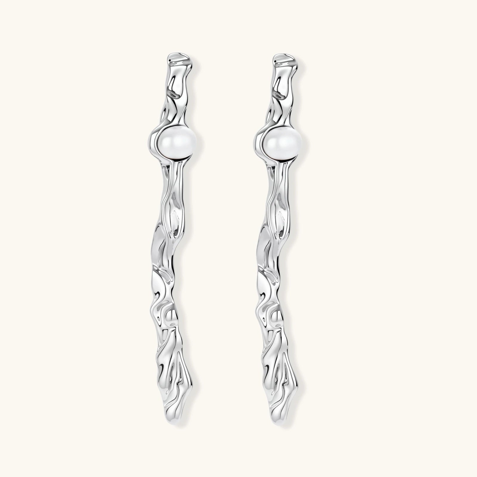 Sculptural silver drop earrings with flowing twisted design and white pearls on neutral background.