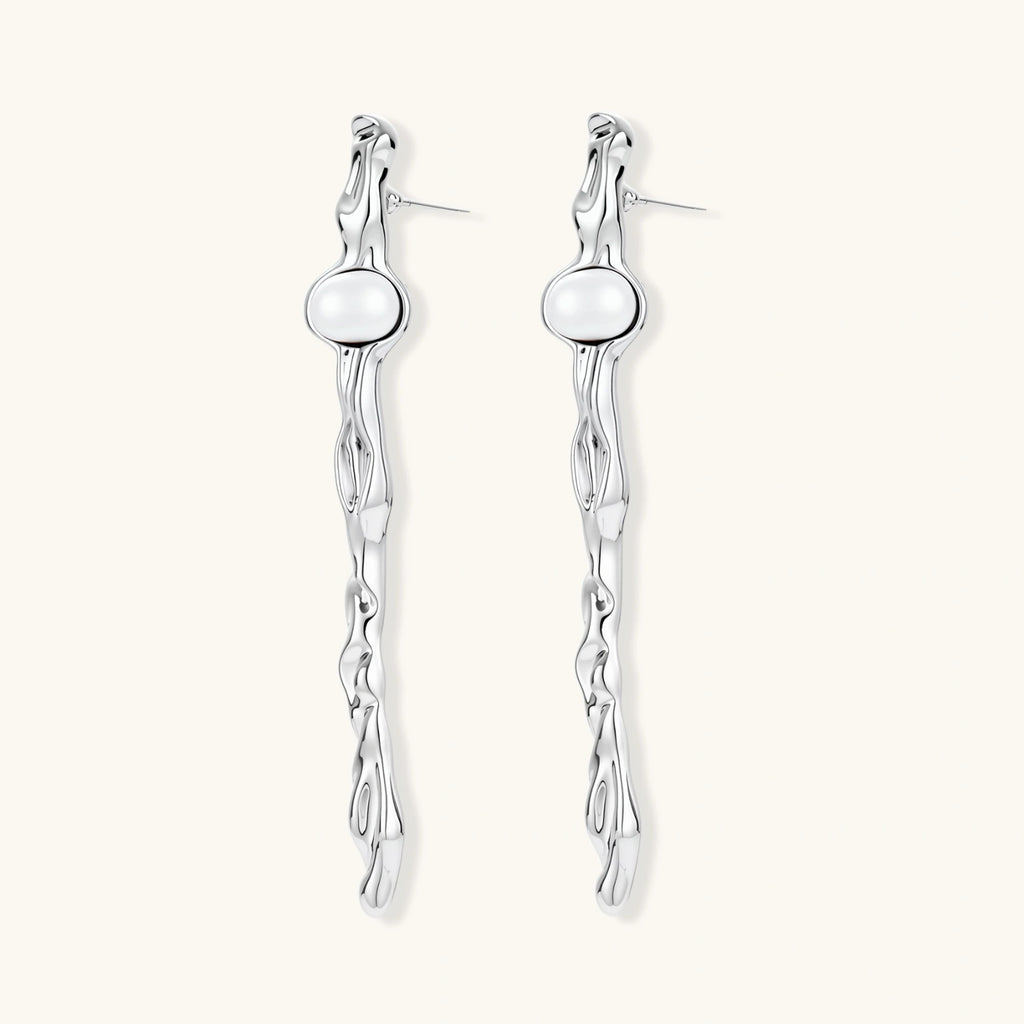 Sculptural silver drop earrings with flowing twisted design and white pearls on neutral background.