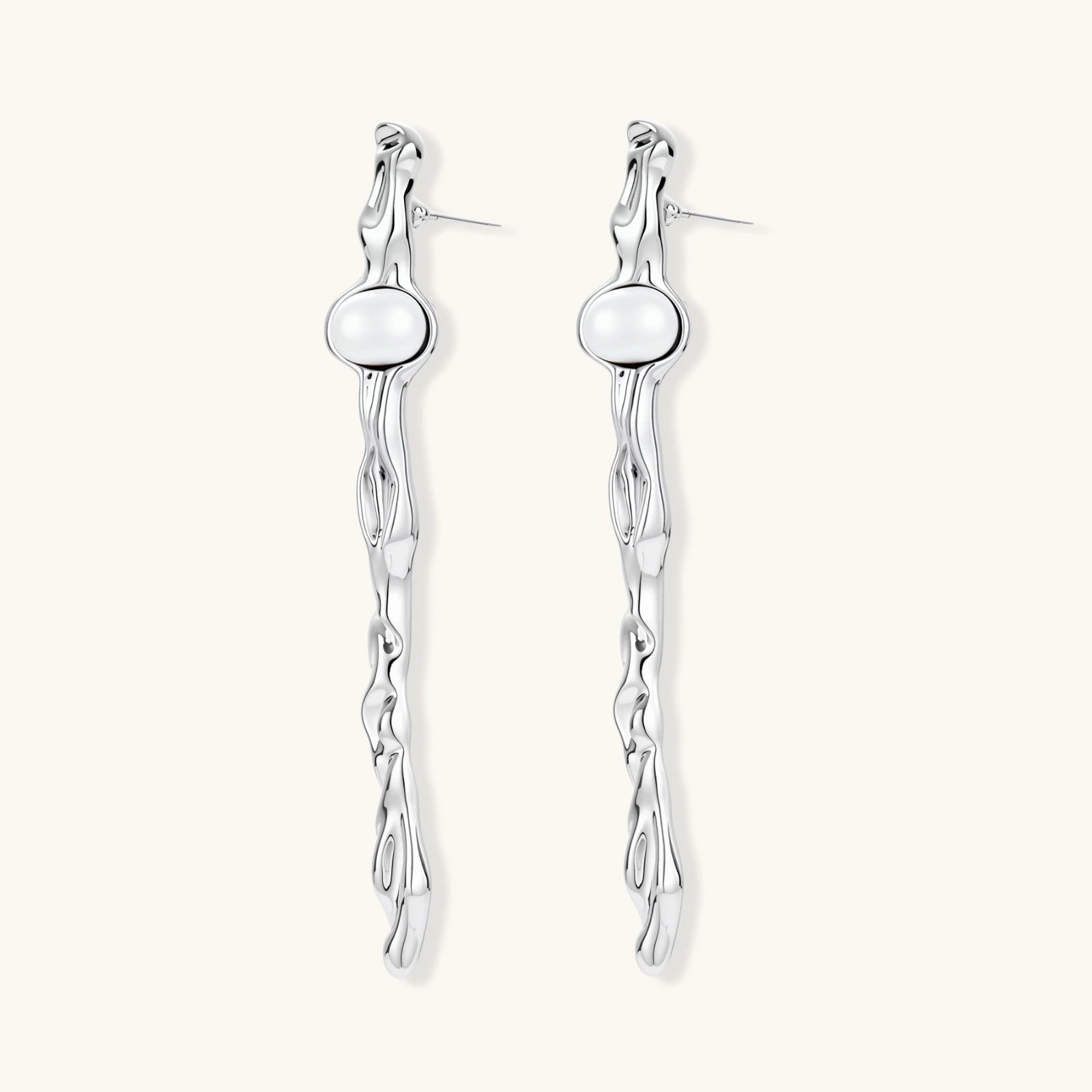 Sculptural silver drop earrings with flowing twisted design and white pearls on neutral background.
