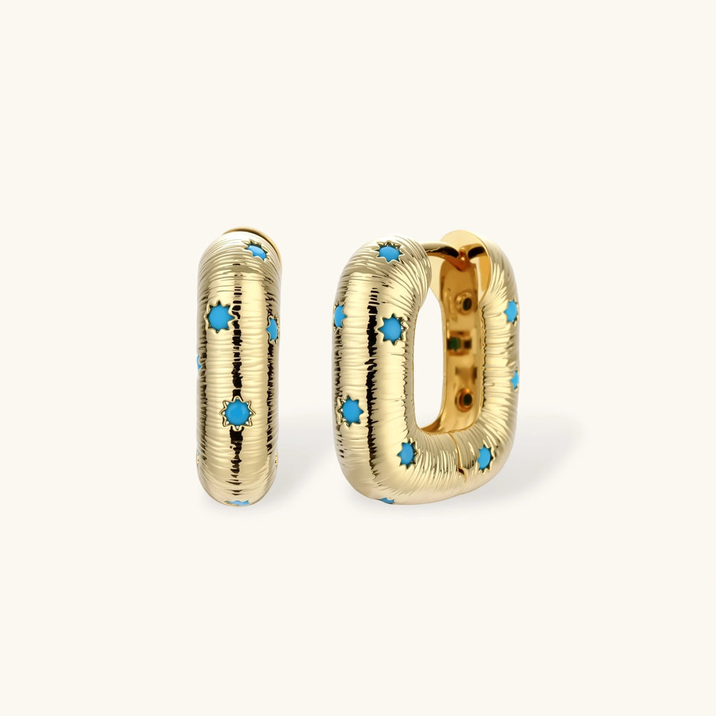 Gold-plated huggie hoop earrings with blue star inlays and textured surface, shown against white background.