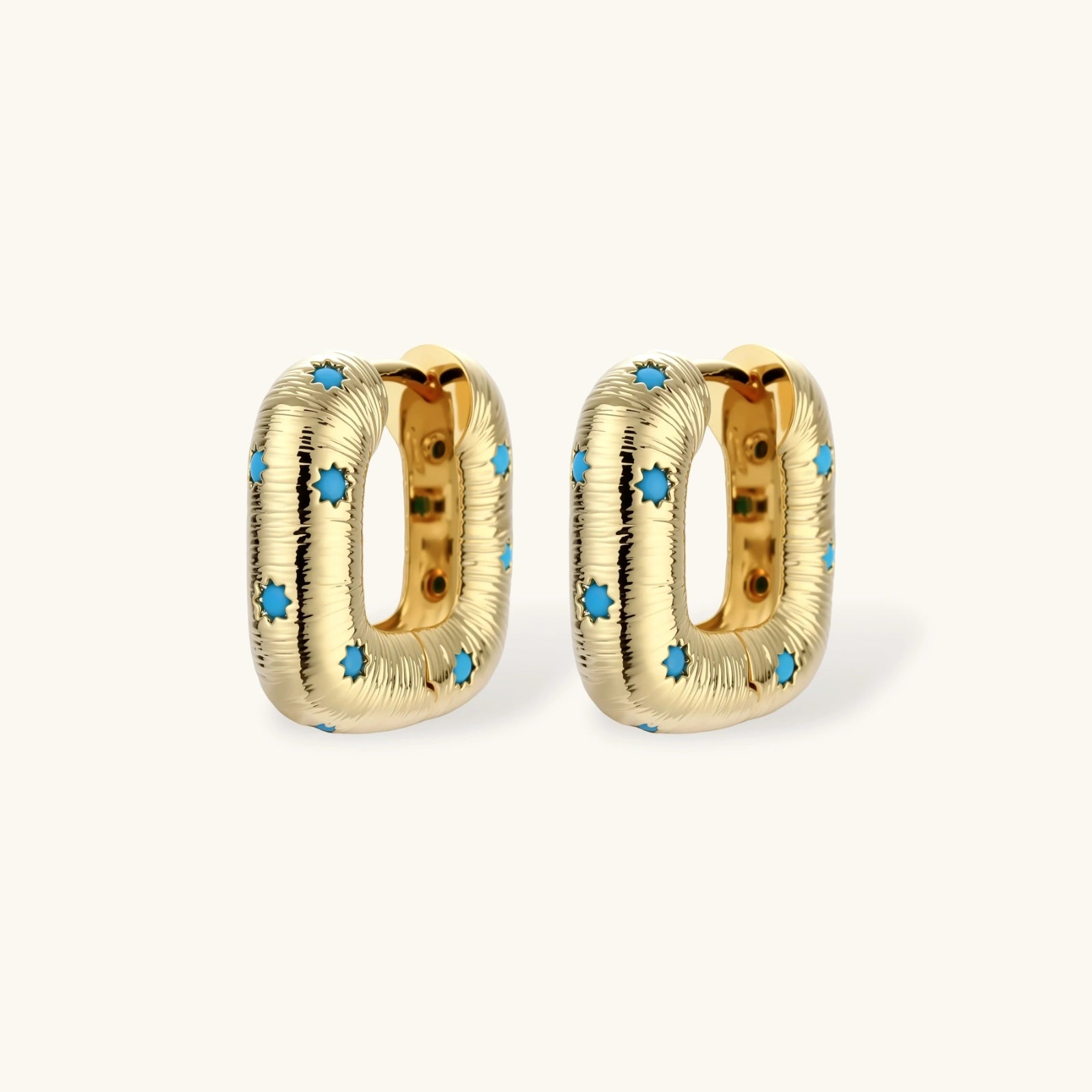 Gold-plated huggie hoop earrings with blue star inlays and textured surface, shown against white background.