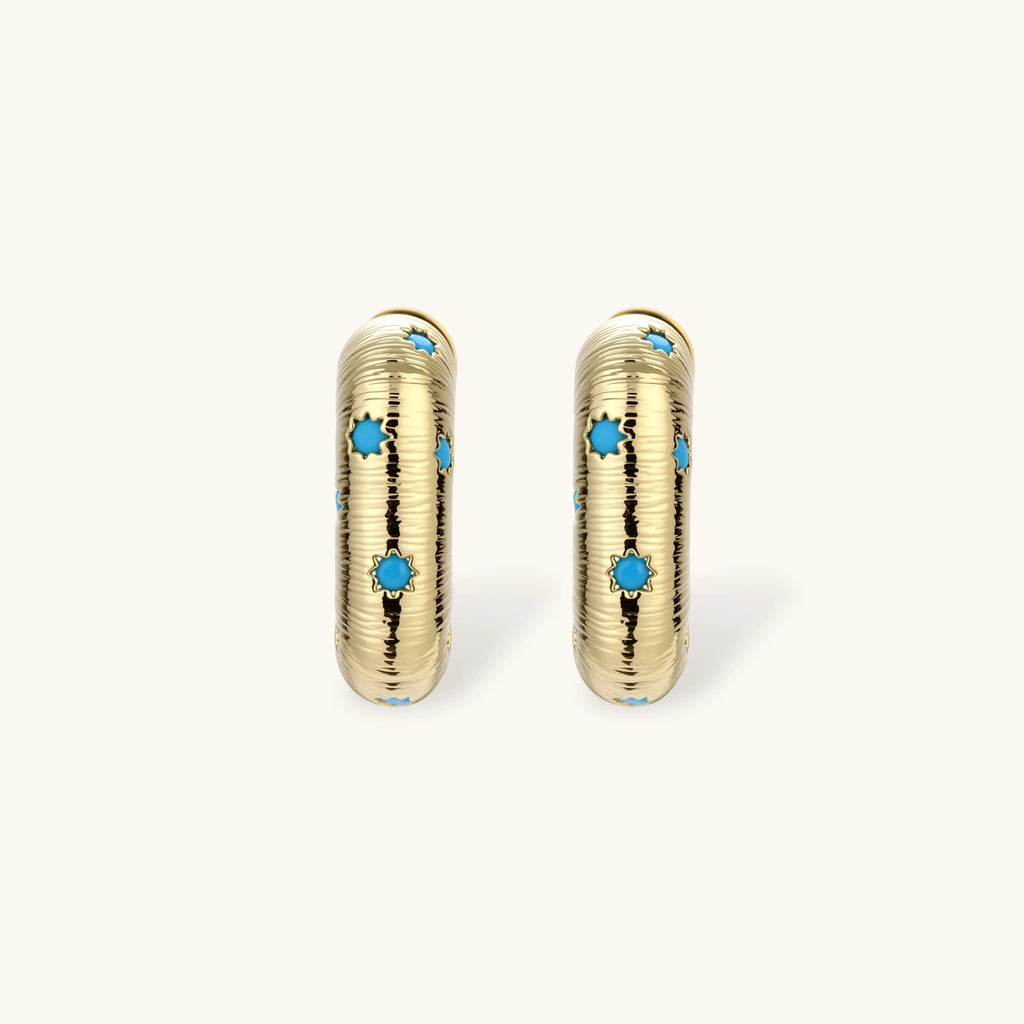 Gold-plated huggie hoop earrings with blue star inlays and textured surface, shown against white background.