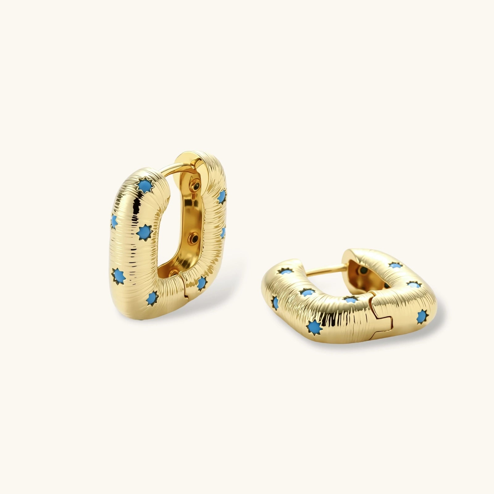 Gold-plated huggie hoop earrings with blue star inlays and textured surface, shown against white background.