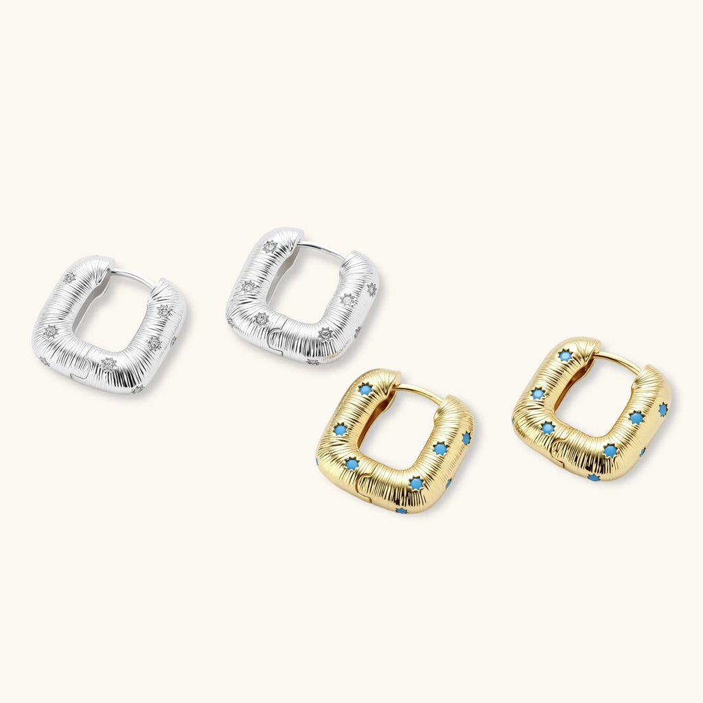 Gold-plated huggie hoop earrings with blue star inlays and textured surface, shown against white background.