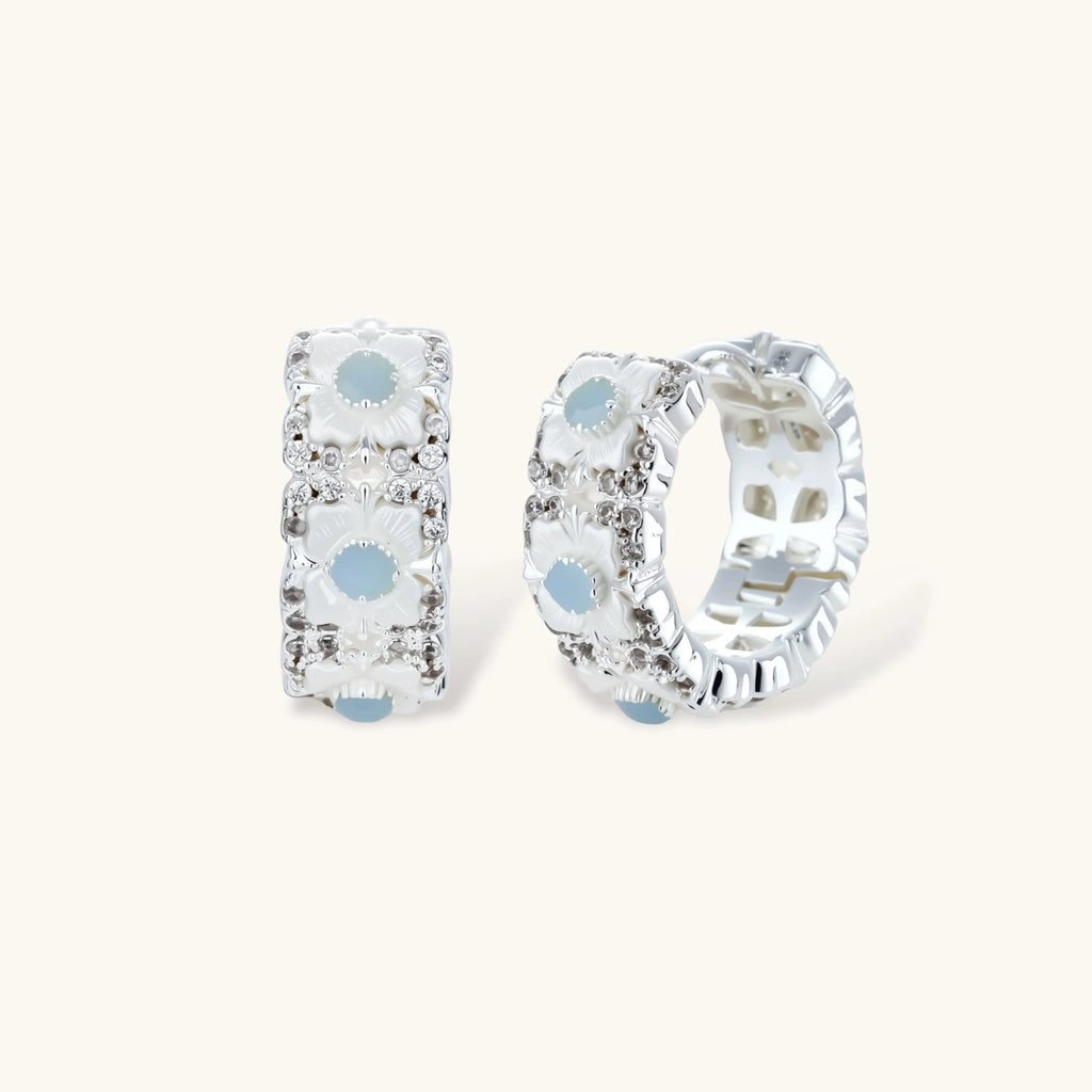 Silver-plated hoop earrings featuring delicate daisy flowers with powder blue centers and crystal accents on white background.