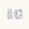 Silver-plated hoop earrings featuring delicate daisy flowers with powder blue centers and crystal accents on white background.