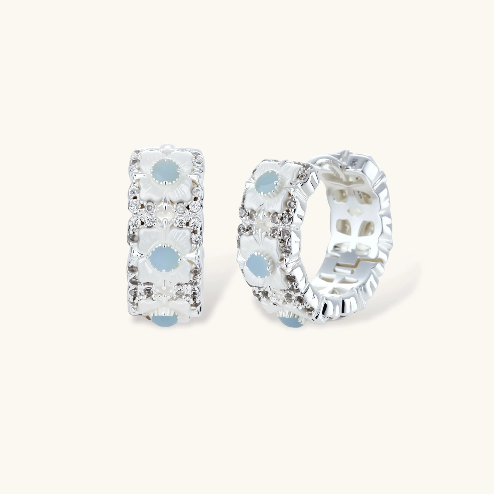 Silver-plated hoop earrings featuring delicate daisy flowers with powder blue centers and crystal accents on white background.