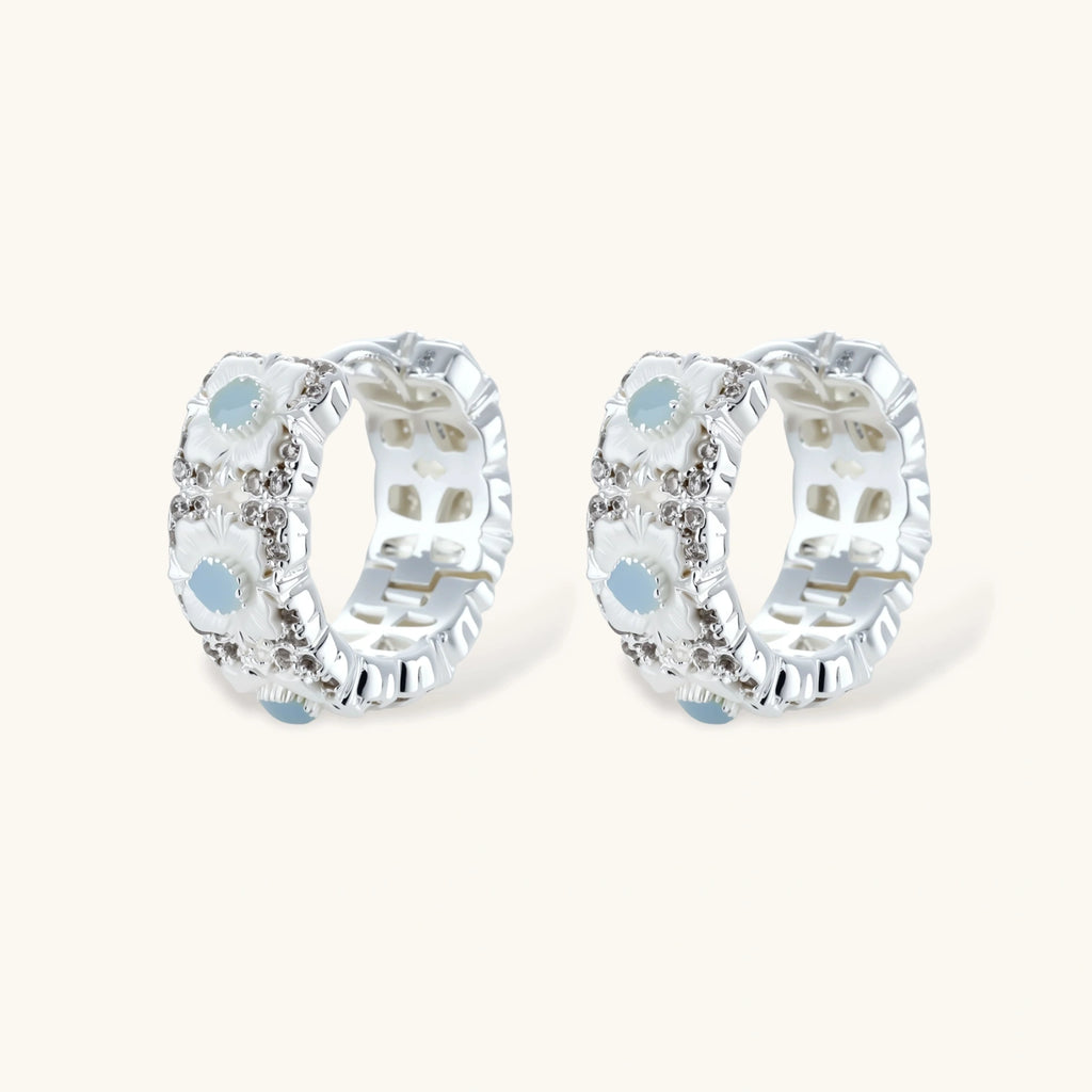 Silver-plated hoop earrings featuring delicate daisy flowers with powder blue centers and crystal accents on white background.