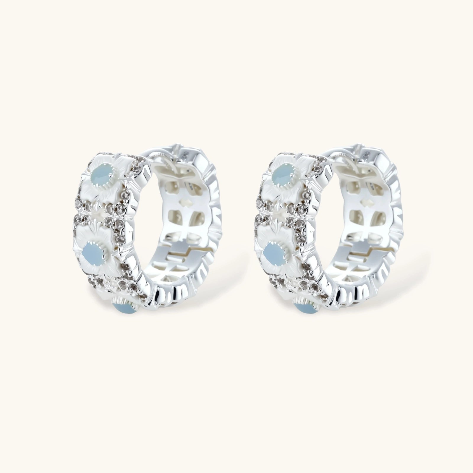 Silver-plated hoop earrings featuring delicate daisy flowers with powder blue centers and crystal accents on white background.