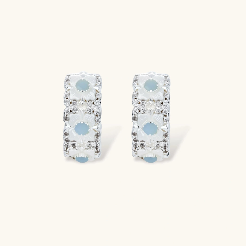 Silver-plated hoop earrings featuring delicate daisy flowers with powder blue centers and crystal accents on white background.
