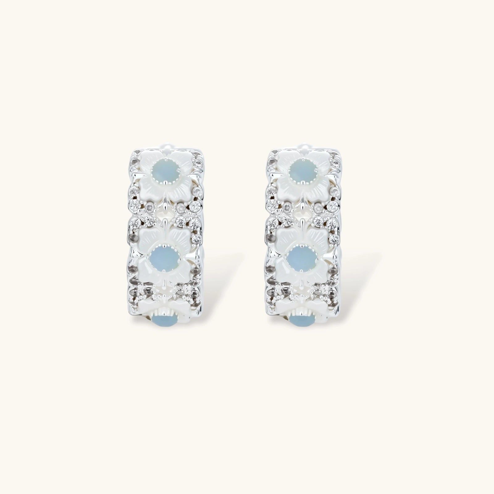 Silver-plated hoop earrings featuring delicate daisy flowers with powder blue centers and crystal accents on white background.