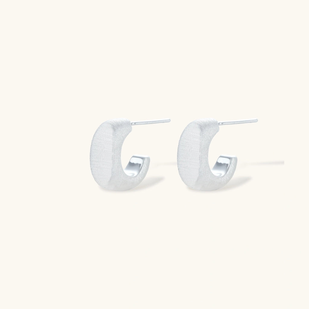 Pair of small silver-plated huggie hoop earrings with clean minimal design on neutral background.