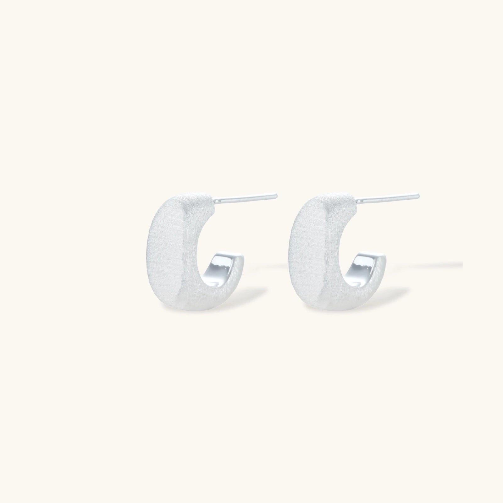 Pair of small silver-plated huggie hoop earrings with clean minimal design on neutral background.