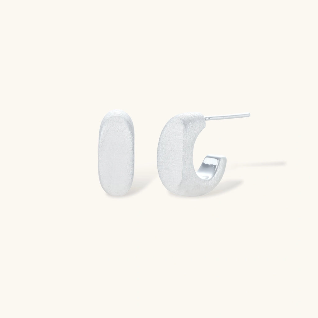 Pair of small silver-plated huggie hoop earrings with clean minimal design on neutral background.