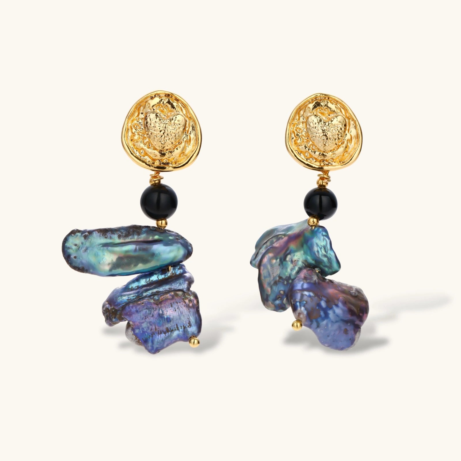 Ornate gold-plated drop earrings with black beads and iridescent blue-purple baroque pearls against white background.