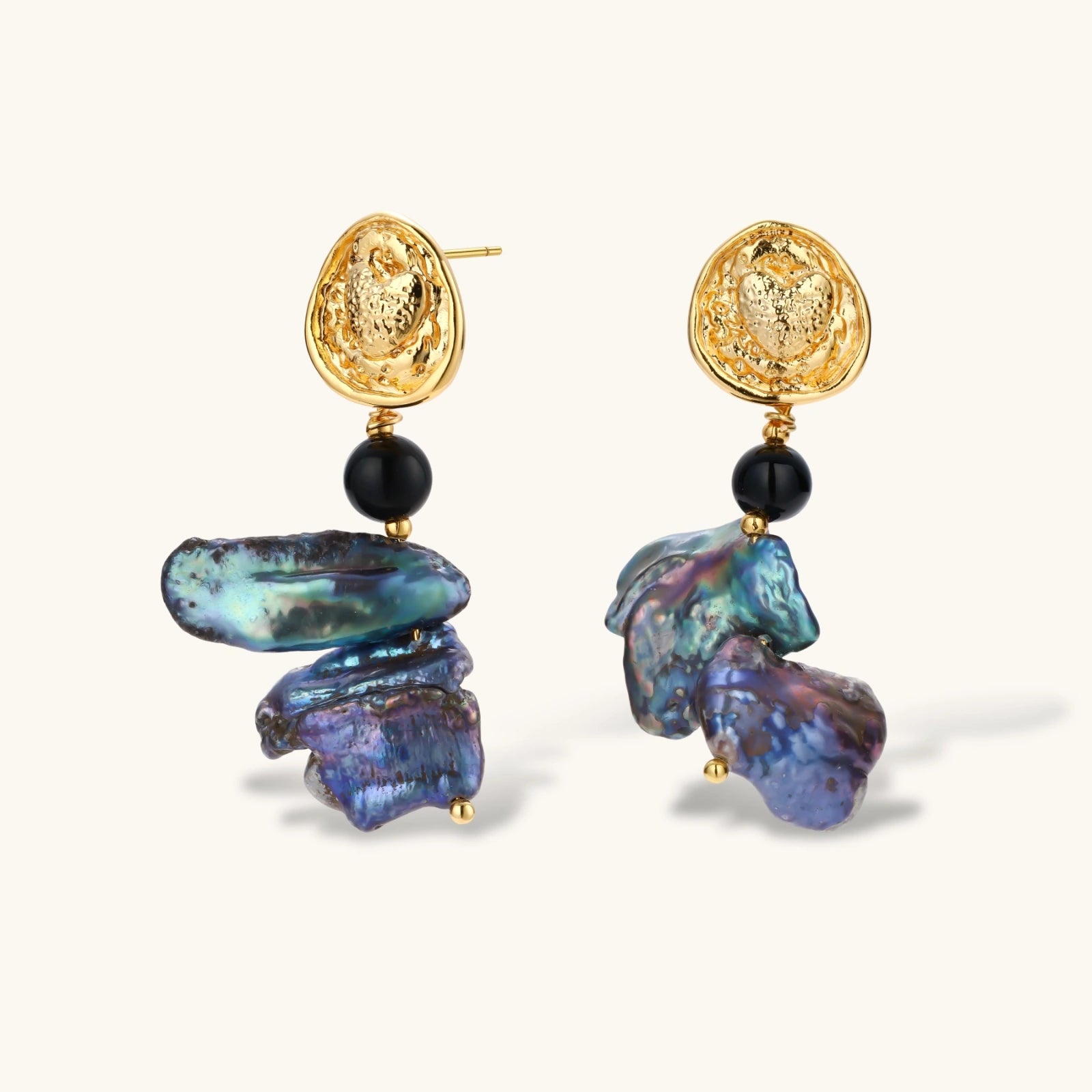 Ornate gold-plated drop earrings with black beads and iridescent blue-purple baroque pearls against white background.