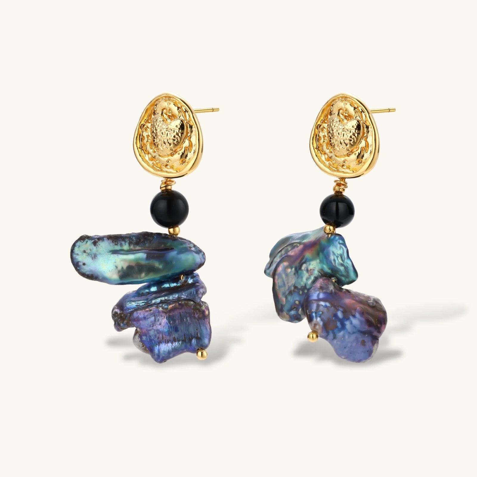 Ornate gold-plated drop earrings with black beads and iridescent blue-purple baroque pearls against white background.