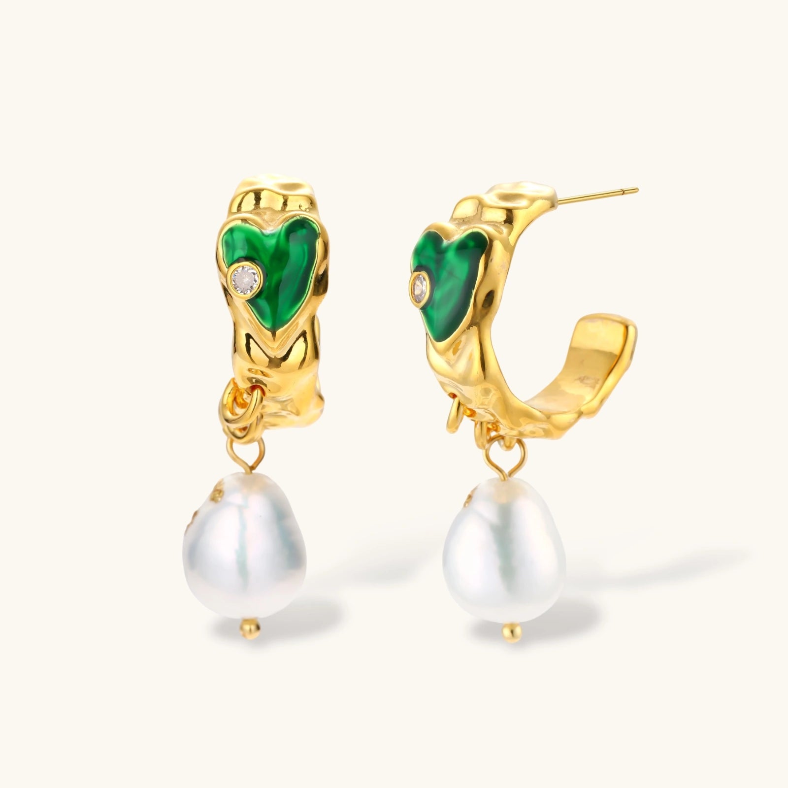 Gold-plated drop earrings with green heart charms and baroque freshwater pearls on neutral background.