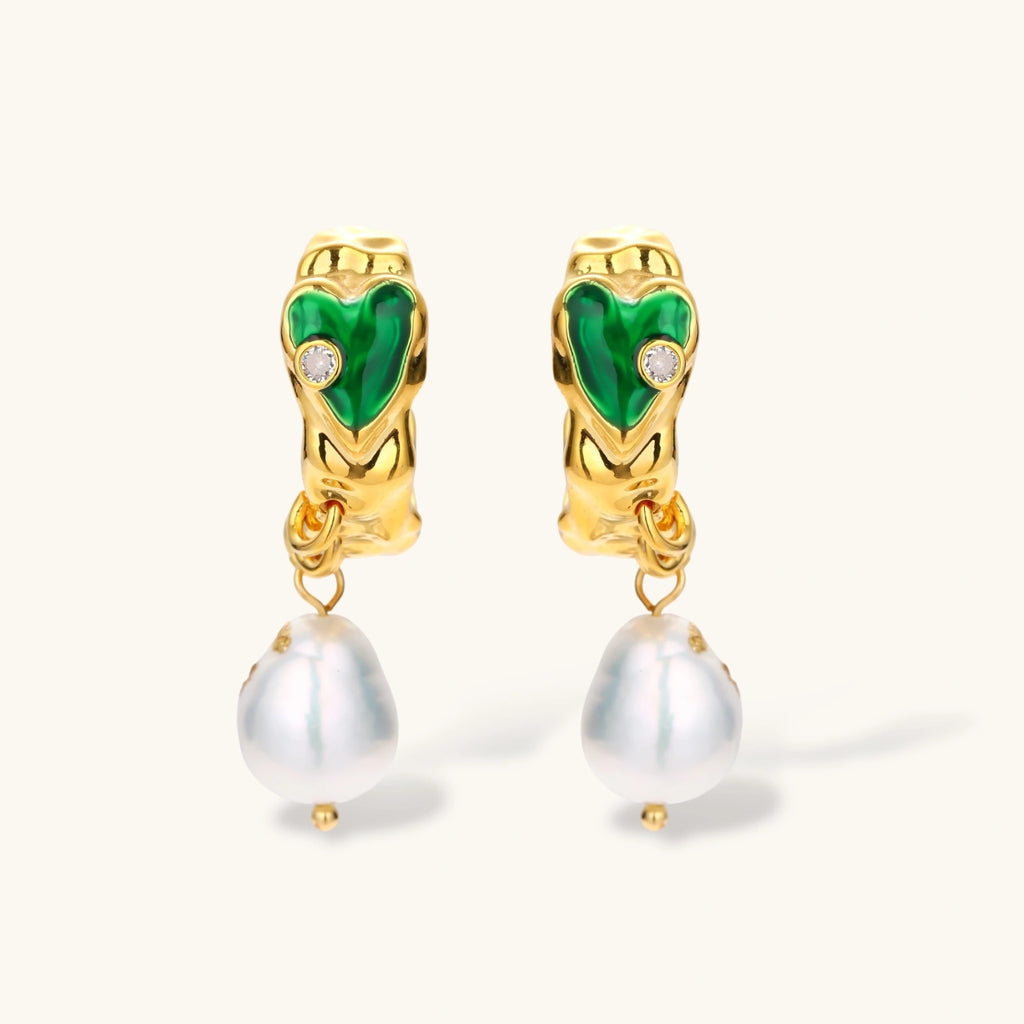 Gold-plated drop earrings with green heart charms and baroque freshwater pearls on neutral background.