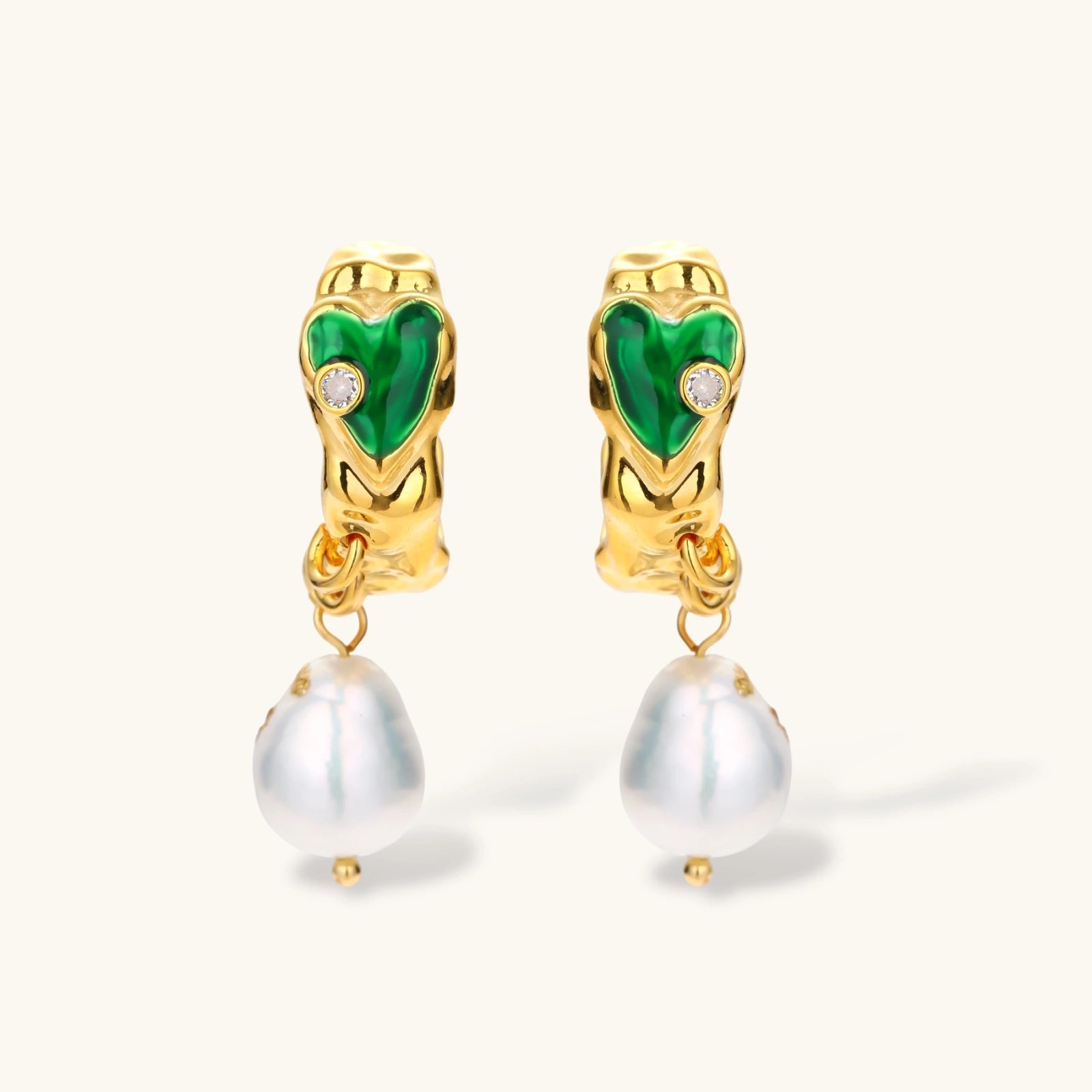 Gold-plated drop earrings with green heart charms and baroque freshwater pearls on neutral background.
