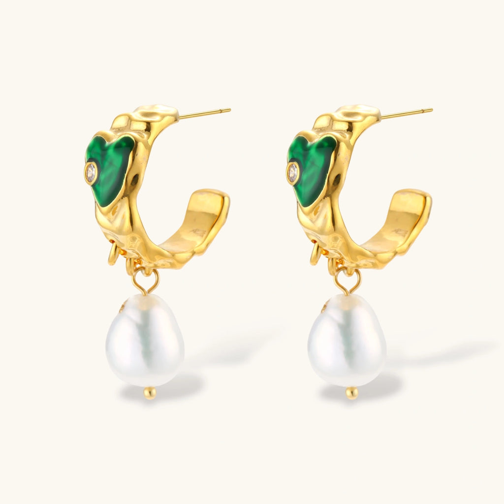 Gold-plated drop earrings with green heart charms and baroque freshwater pearls on neutral background.