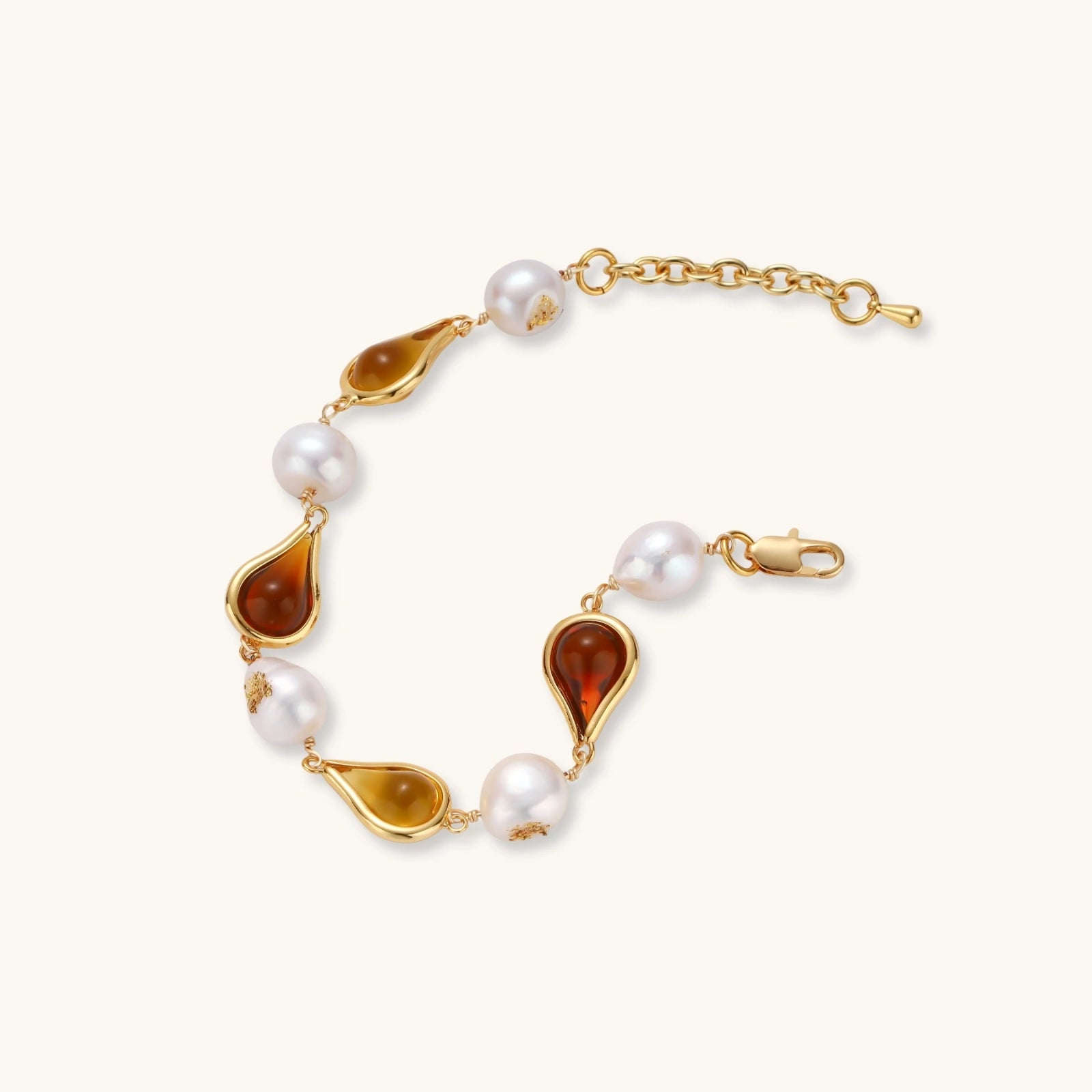 Elegant bracelet with alternating baroque pearls and amber teardrop gemstones set in 18k gold-plated copper on cream background.