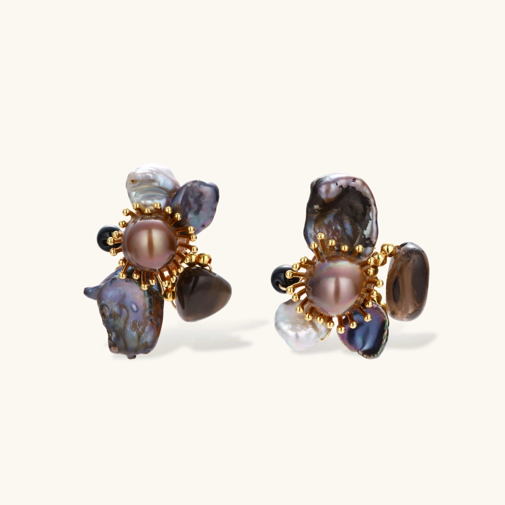 Dark baroque pearl cluster earrings with gold sunburst centers arranged in organic floral design on cream background.