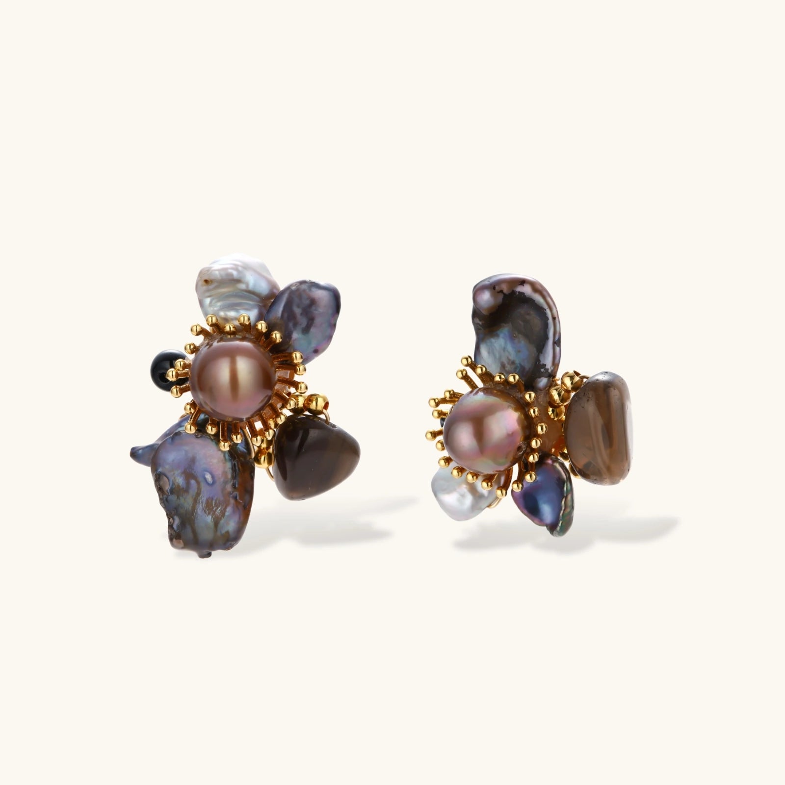 Dark baroque pearl cluster earrings with gold sunburst centers arranged in organic floral design on cream background.