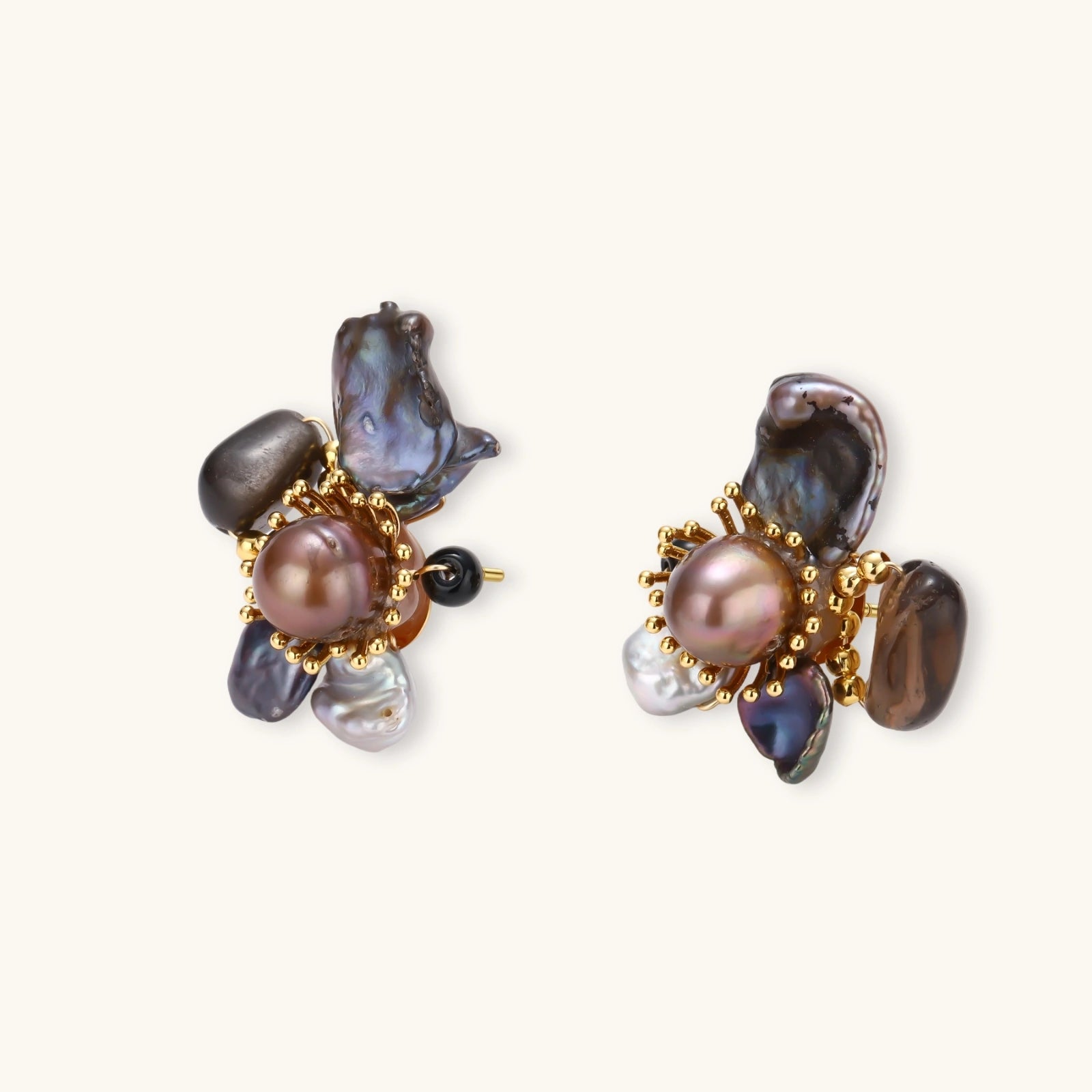 Dark baroque pearl cluster earrings with gold sunburst centers arranged in organic floral design on cream background.