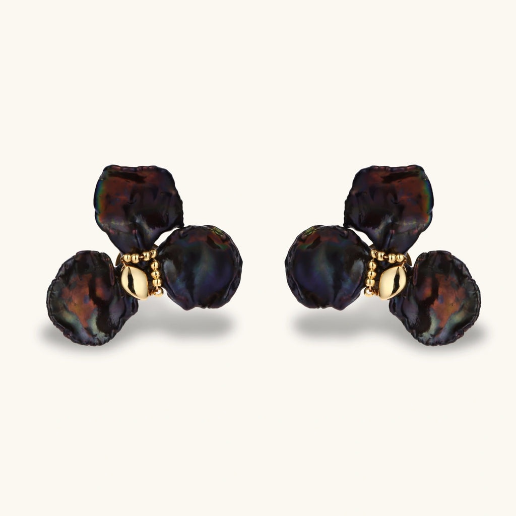 Dark iridescent baroque pearls arranged in flower pattern with 18K gold-plated center on cream background.