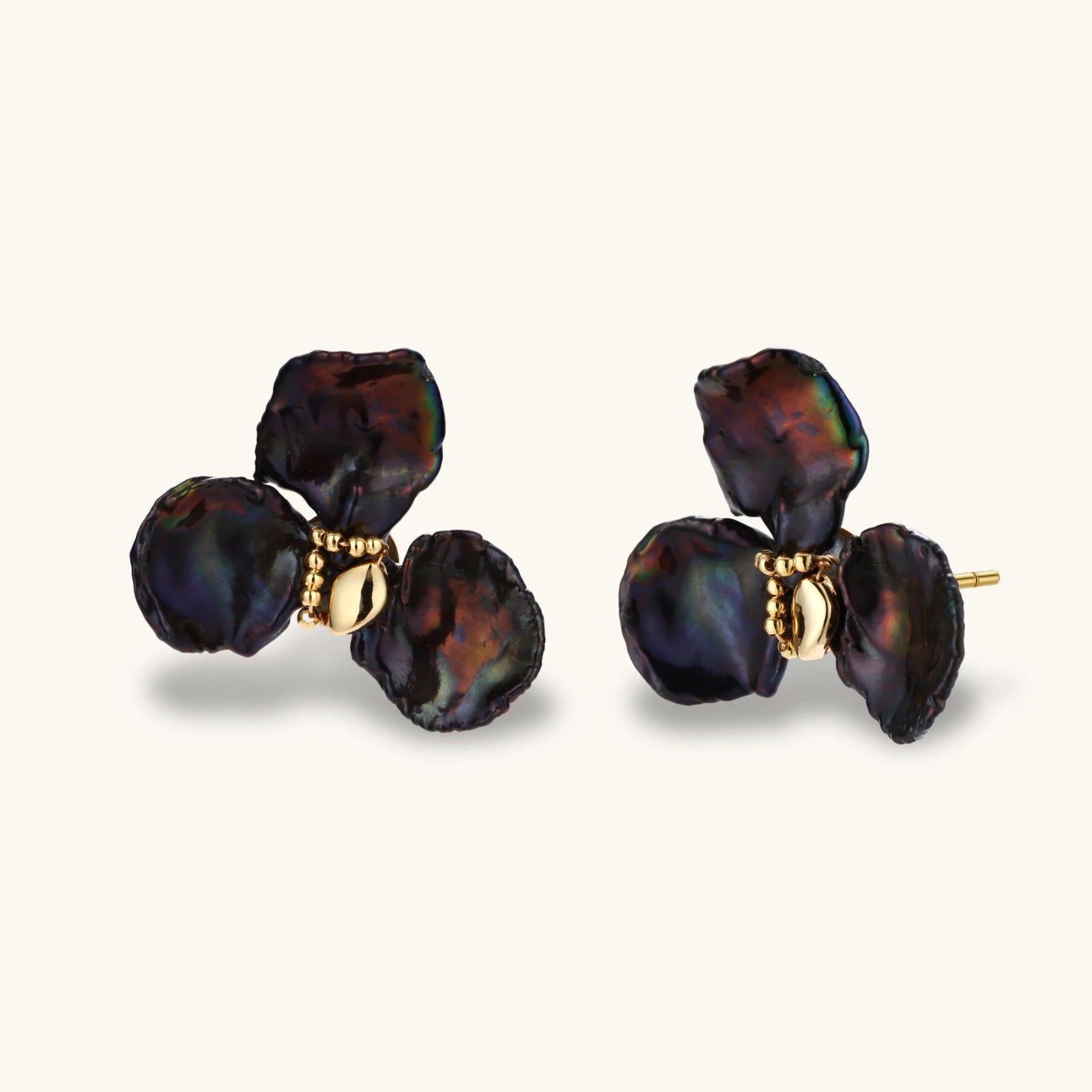 Dark iridescent baroque pearls arranged in flower pattern with 18K gold-plated center on cream background.