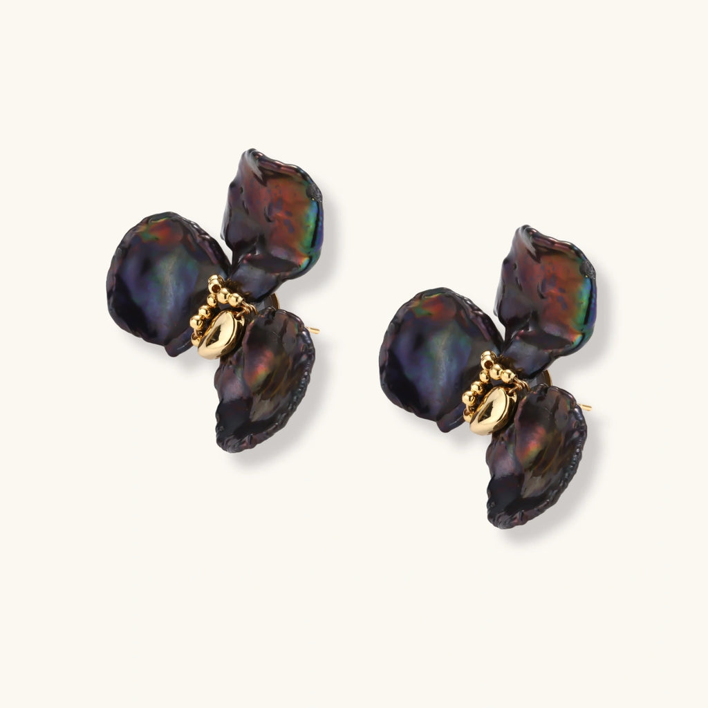 Dark iridescent baroque pearls arranged in flower pattern with 18K gold-plated center on cream background.
