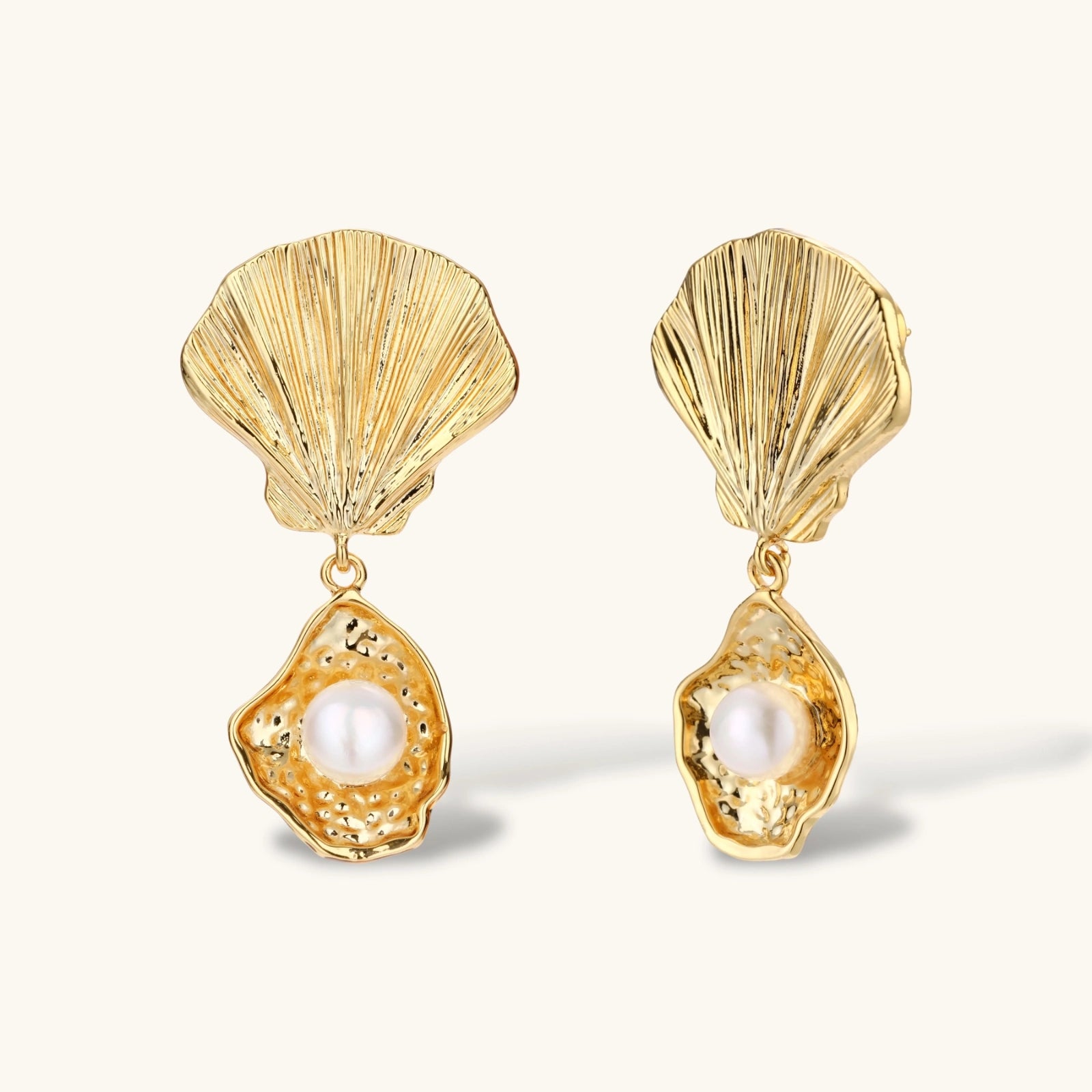 Gold shell-shaped drop earrings with scallop tops and oyster bottoms featuring round freshwater pearls on white background.