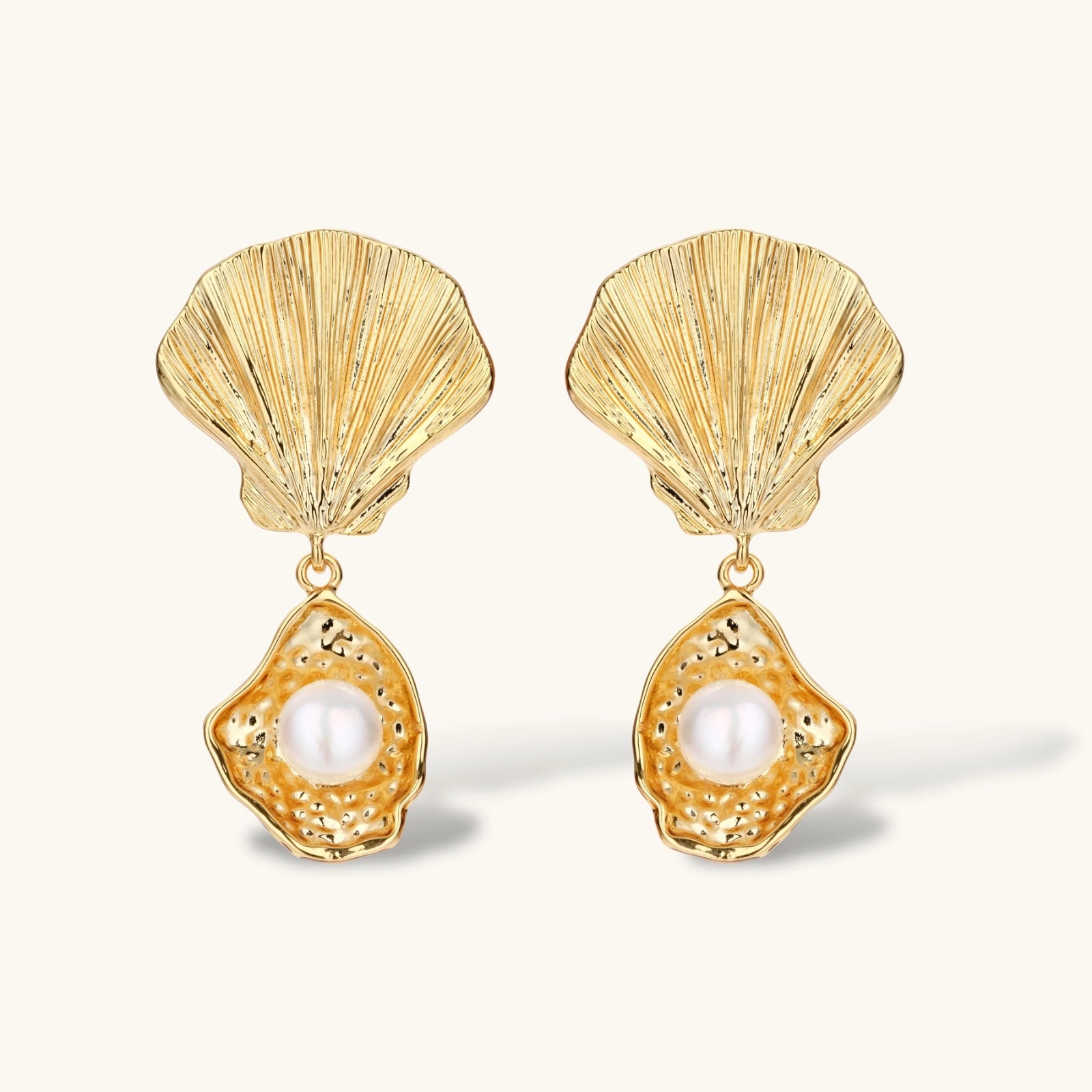 Gold shell-shaped drop earrings with scallop tops and oyster bottoms featuring round freshwater pearls on white background.